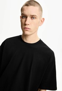 Tricou din bumbac negru, cu guler rotund și mâneci scurte; are o croială lejeră și o textură netedă. Fără modele sau accente vizibile.