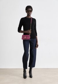 Un pull noir, un jean cropped bleu marine et des bottines noires. Un petit sac bandoulière rose avec un fermoir doré. Des lunettes de soleil portées.