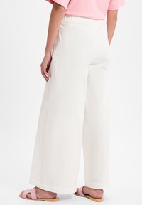 Weiße weite Hosen mit einem elastischen Bund, die eine glatte Textur aufweisen und einen Saum haben, der knapp über dem Knöchel endet, kombiniert mit rosa Sandalen.