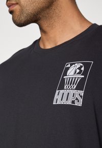 Zwart katoenen T-shirt met een witte grafische print van een basketbal en wereldbolmotief, met het label "HOOPS" op de linkerborst.