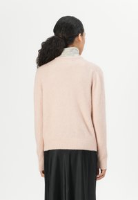 Light pink, fluffy sweater with a round neck and ribbed cuffs. Worn over a black skirt, featuring a striped collar visible underneath.