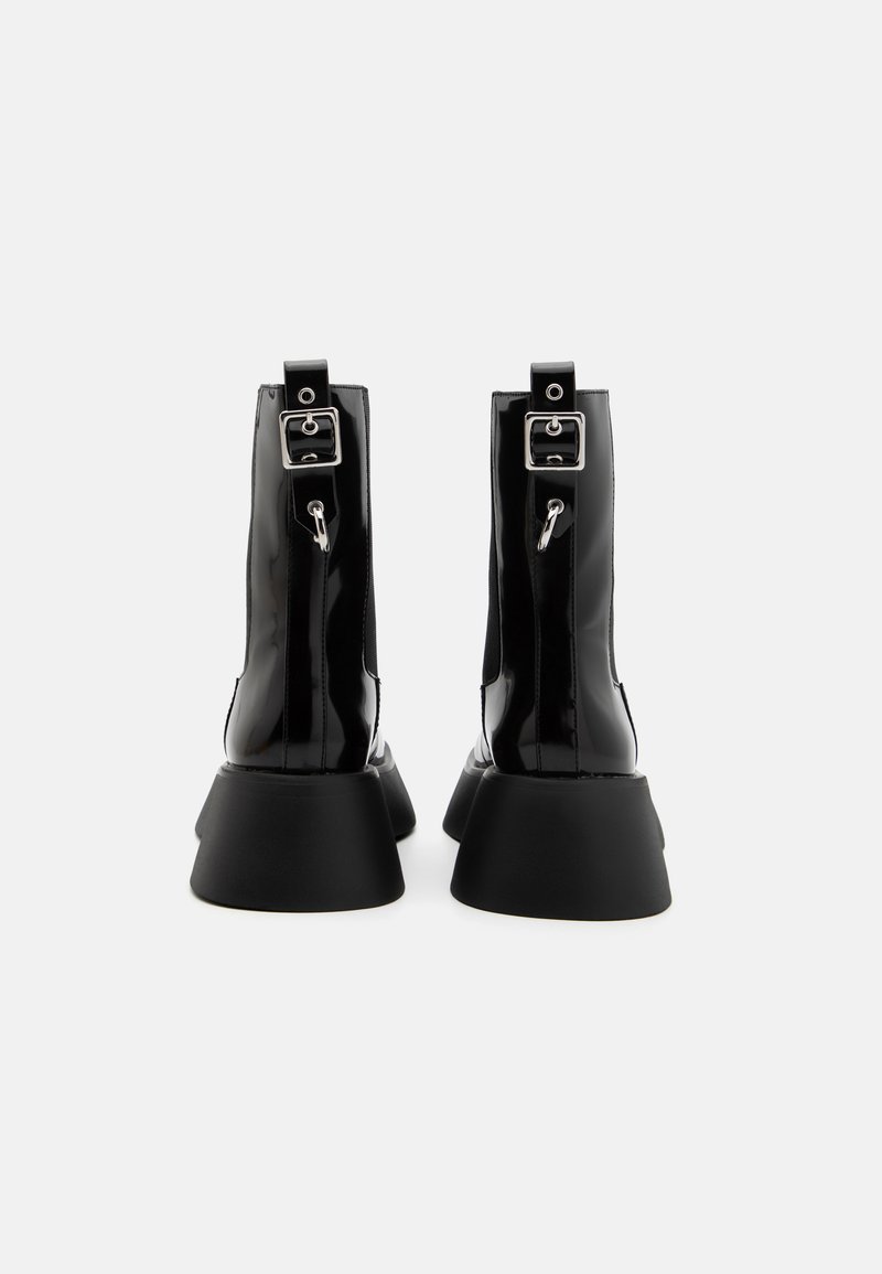 Czarne, lakierowane botki za kostkę z masywną czarną platformą, wyposażone w srebrne klamry i zamki błyskawiczne z tyłu dla regulowanego dopasowania.