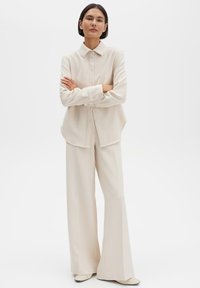 Crèmekleurige blouse met een knoopsluiting aan de voorkant en een afgeronde zoom, gecombineerd met crèmekleurige wijde broekspijpen. Soepel stof en een op maat gemaakt ontwerp.