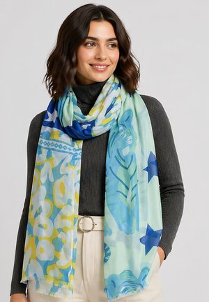 Woman with shoulder-length dark hair wearing a dark ribbed sweater and a colorful blue, yellow, and green patterned scarf.