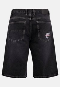 Mustad teksapüksid kahe tagataskuga, ühel kalatikand ja punase tekstiga sõna "REBEL".