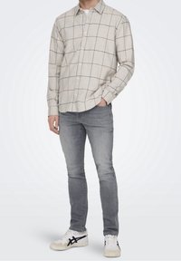 Beige ruudullinen paita nappilistalla, pitkät hihat ja rento malli, yhdistettynä slim-fit harmaisiin farkkuihin ja valkoisiinlenkkareihin.