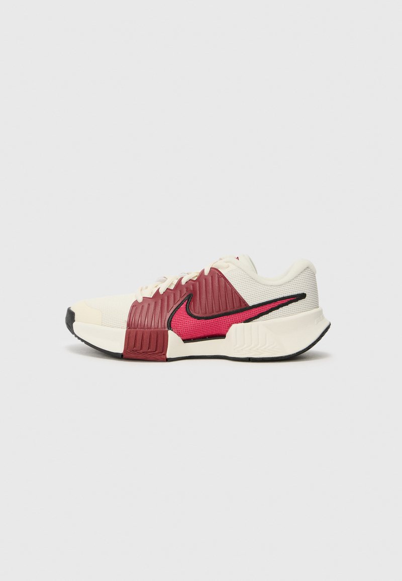 Nike sneakers featuring a cream upper, red textured accents, black detailing, and a patterned midsole. Laced with a cushioned sole design.