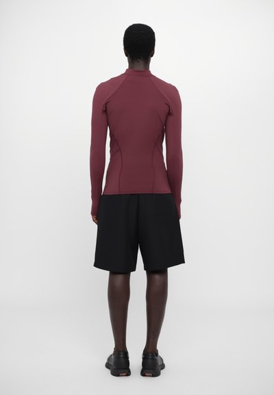 Maroon long-sleeve top with a high collar and fitted design, paired with black shorts. Smooth texture, athletic cut, and simple detailing.