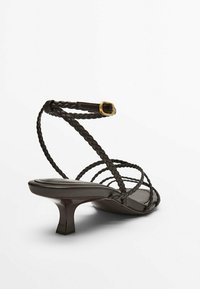 Ruske strappy sandale s pletenim remenima za gležanj i stopalo, niska kitten potpetica i mali zlatni kopčasti remen na remenu oko gležnja.
