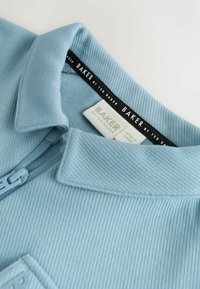 Himmelblaues Poloshirt aus strukturiertem Material, mit Reißverschlusskragen und schwarzem Etikett mit "BAKER by TED BAKER" sowie Größenetikett.