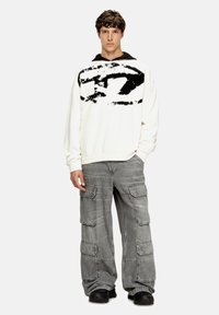 Sudadera blanca con estampado gráfico negro, combinada con pantalones cargo grises que cuentan con múltiples bolsillos y un corte relajado. Zapatillas negras completan el look.