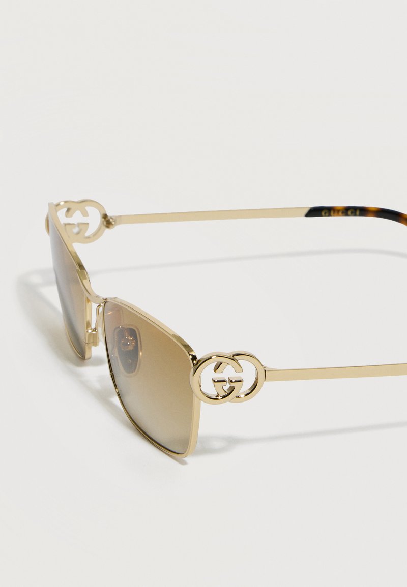 Lunettes de soleil à monture dorée avec verres dégradés marron et logo double G entrelacé sur les branches.