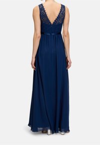 Marinblå aftonklänning med spetsbak, ärmlös design och flödande kjol. Har en V-formad rygg och ett satinband i midjan.