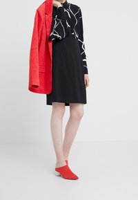 Svart klänning med vitt abstrakt mönster, matchad med en röd kordflodjacka och röda klackar med kraftig klack. Slätt tyg och skräddarsydd passform.