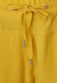 Geel trekkoord tailleband met een geknoopt strikje. Gladde stof met zichtbare stiksels. Metalen toggles aan de trekkoorden met een casual, ontspannen ontwerp.