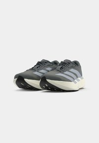 Zapatillas deportivas grises con suelas gruesas que presentan acentos negros, rayas grises a los lados y una parte superior texturizada. Diseño de cordones con ojales reforzados.