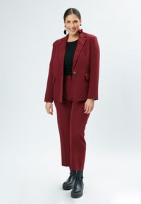 Completo giacca e pantaloni borgogna realizzato in tessuto liscio, con chiusura a un bottone, rever affilati e tasche laterali. Stivali platform neri.