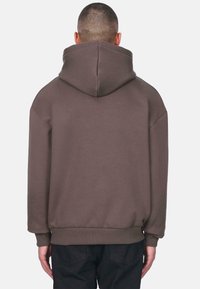 Brun oversized hoodie med en stor hætte, ribbede manchetter og talje. Blød tekstur; ingen synlige logoer eller mønstre på ryggen.