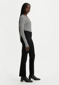 Top de manga larga a rayas en blanco y negro, combinado con jeans negros ajustados y botines negros, mostrado en un modelo de perfil.