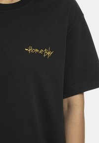 Juodas medvilninis marškinėliai su geltonu siuvinėjimu "HomeBoy" kairiajame krūtinės šone. Trumpomis rankovėmis ir apvaliu iškirpimu.