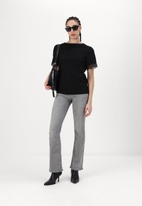 Svart kortermet topp med blonderkant, grå vide jeans og svarte hælekorte støvler. Bærer en svart håndveske og har på seg solbriller.