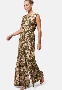 Combinaison florale en vert olive, avec un décolleté en V, sans manches, des jambes larges fluides, et un mélange de motifs de fleurs crème et jaunes.