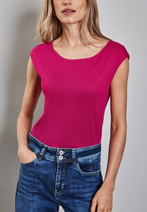 Top rosa ajustado sin mangas con escote redondeado, combinado con jeans de mezclilla azul que cuentan con cierre de dos botones y bolsillos frontales.