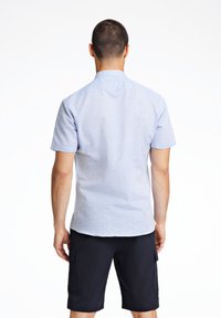 Camicia a maniche corte con bottoni di colore azzurro chiaro con un motivo texturizzato, abbinata a pantaloni corti scuri con tasche cargo e taglio dritto.