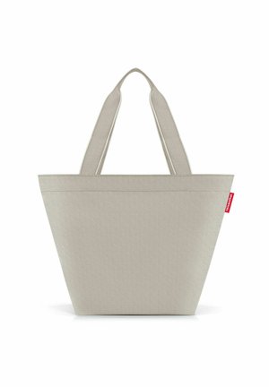 Sac en toile beige avec deux larges poignées, de forme triangulaire, surface texturée et une petite étiquette logo rouge sur le côté.