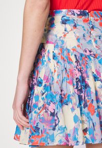 Jupe à imprimé floral présentant des nuances de bleu, rose et orange, avec des plis et une fermeture éclair à la taille, fabriquée en tissu léger.