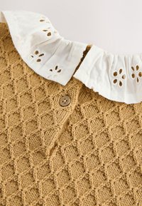 Gilet marron en maille avec motif losange et bouton, avec un col blanc à volants orné de broderies florales découpées.