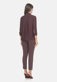 Blusa bordeaux con una vestibilità comoda, maniche arrotolate e spacchi laterali, abbinata a pantaloni bordeaux sartoriali e scarpe con tacchi alti.