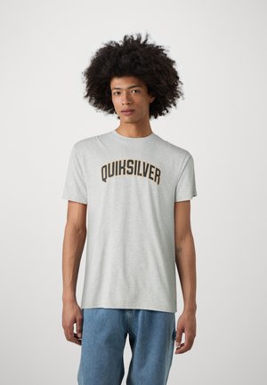 Grijze katoenen T-shirt met korte mouwen, met een zwart en gouden "QUIKSILVER" logo op de borst. Model draagt blauwe jeans.