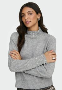 Grå genser med ribbestrikket høy hals, prydet med små falske perler på skuldre og ermer, med strukturert strikk og tettsittende design.