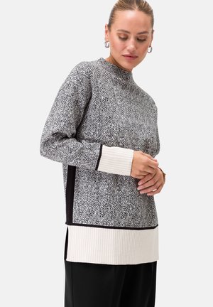 Knitted pullover with a herringbone pattern in black and white, featuring ribbed cuffs and a side slit in a slightly longer silhouette.