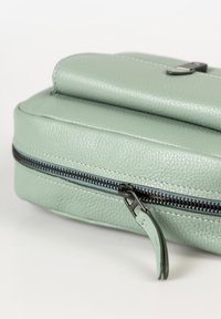 Borsa in pelle verde con superficie texturizzata, caratterizzata da una cerniera scura e un robusto tassello per il tiraggio. Forma rettangolare compatta con linee morbide.