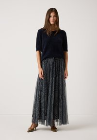 Navyblauer, fuzzie Kurzarm-Pullover kombiniert mit einem langen, gemusterten Tüllrock in Marineblau und Weiß. Beigefarbene Absatzschuhe vervollständigen das Outfit.