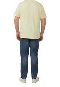 Lichtgele T-shirt met korte mouwen en blauwe denim jeans. T-shirt heeft een ronde hals; jeans hebben een rechte pasvorm en een vervaagde structuur. Casual schoenen.