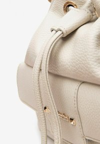 Borsa a secchiello in pelle beige con finitura testurizzata, chiusura a coulisse, hardware dorato e dettaglio con logo sul lato.