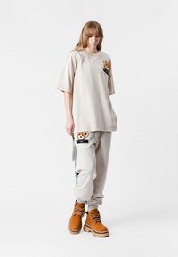 Camiseta oversize beige con un parche de oso, combinada con joggers beige claros con bolsillos y botas marrones con cordones.