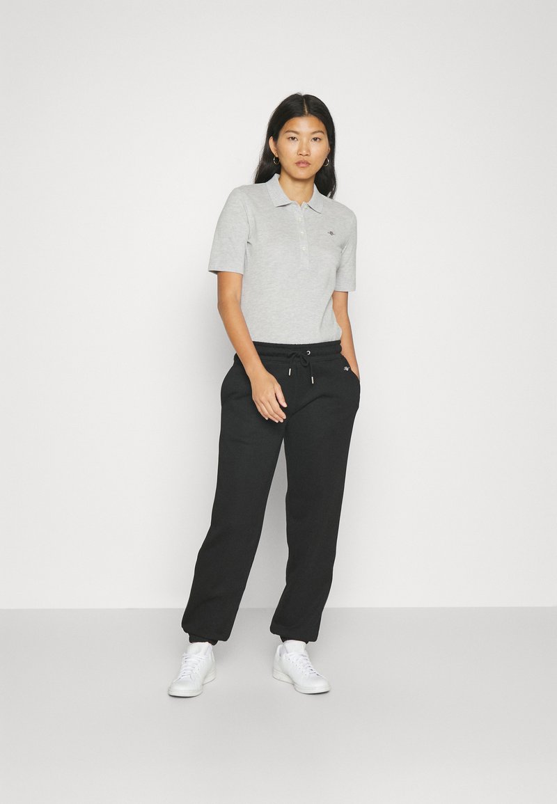 Jasnoszara koszulka polo z krótkim rękawem i kołnierzykiem, połączona z czarnymi spodniami dresowymi z elastycznym pasem i białymi sneakersami.