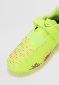 Neon gule treningssko med en teksturert overflate, med et rosa og svart grafisk mønster og en enkelt justerbar stropp over toppen.
