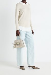 Beige top met lange mouwen en een ronde hals, eronder een wit overhemd, lichtblauwe wijde jeans, beige tas met veters en metallic puntige schoenen.