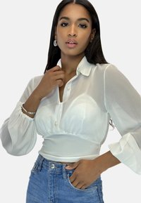 Witte blouse met pofmouwen, een knoopsluiting aan de halslijn en een textuurstof, gecombineerd met lichtblauwe denim jeans. De blouse heeft een getailleerde taille.