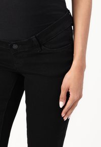 Jeans de mezclilla negros con un corte clásico, que cuentan con un cierre de botón, lazos para el cinturón y bolsillos frontales. La textura parece suave con un ligero estiramiento.
