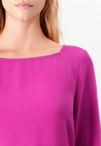Violetti paita suoralla pääntiellä, jonka materiaalina on teksturoitu kangas. Varustettu pitkähihaisilla hihoilla ja sileällä pinnalla.