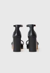Czarne sandały na wysokim obcasie typu słupek. Posiadają paski wokół kostki i otwarty nosek, wykonane z gładkiej skóry.