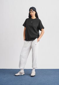 Juoda Nike trumpomis rankovėmis marškinėliai, pilkos laisvalaikio kelnės su šoninėmis kišenėmis ir šviesiai pilki batai su juodu „90“ akcentu. Paprastas, kasdienis dizainas.