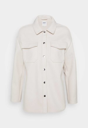 Veste boutonnée de couleur crème avec deux poches poitrine et manches longues, dotée d'un col classique et de boutons-pression en métal sur le devant.