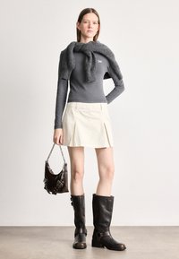 Γκρι μακρυμάνικο μπλουζάκι, μπεζ πλισέ μίνι φούστα, γκρι σάλι ριγμένο στους ώμους, καφέ δερμάτινες μπότες μέχρι το γόνατο και καφέ τσάντα χειρός με αλυσίδες.